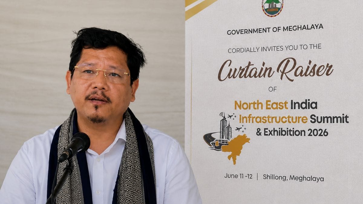 Meghalaya Chief Minister Conrad Sangma beside the official poster of the North East India Infrastructure Summit & Exhibition 2026 in Shillong.